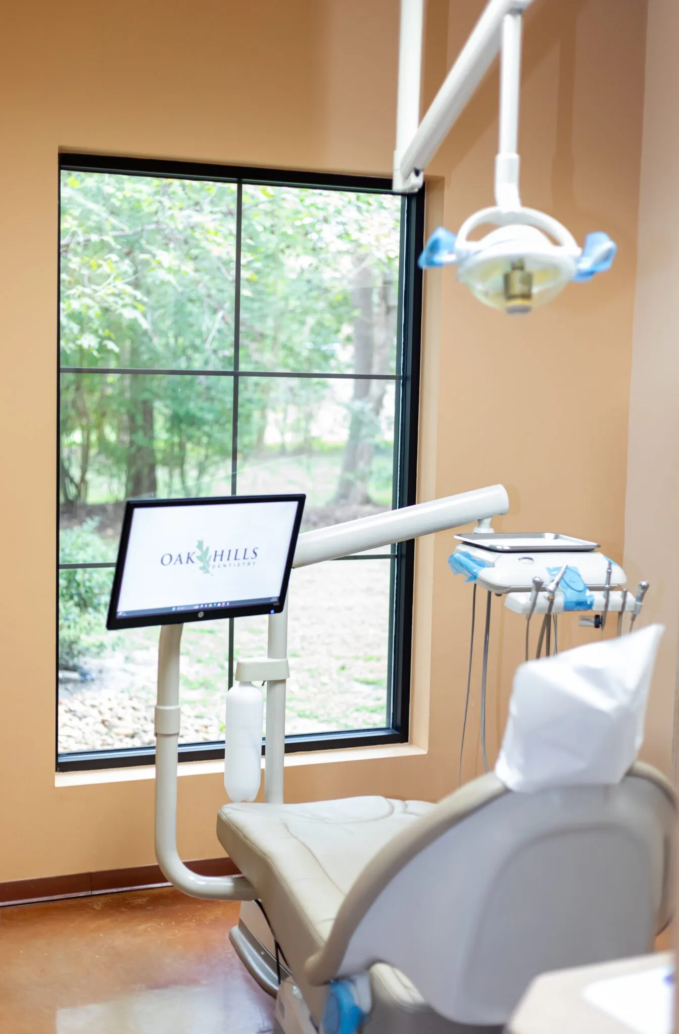A treatment room at Oak Hills Dentistry with the chair set beside a full-height window looking onto trees